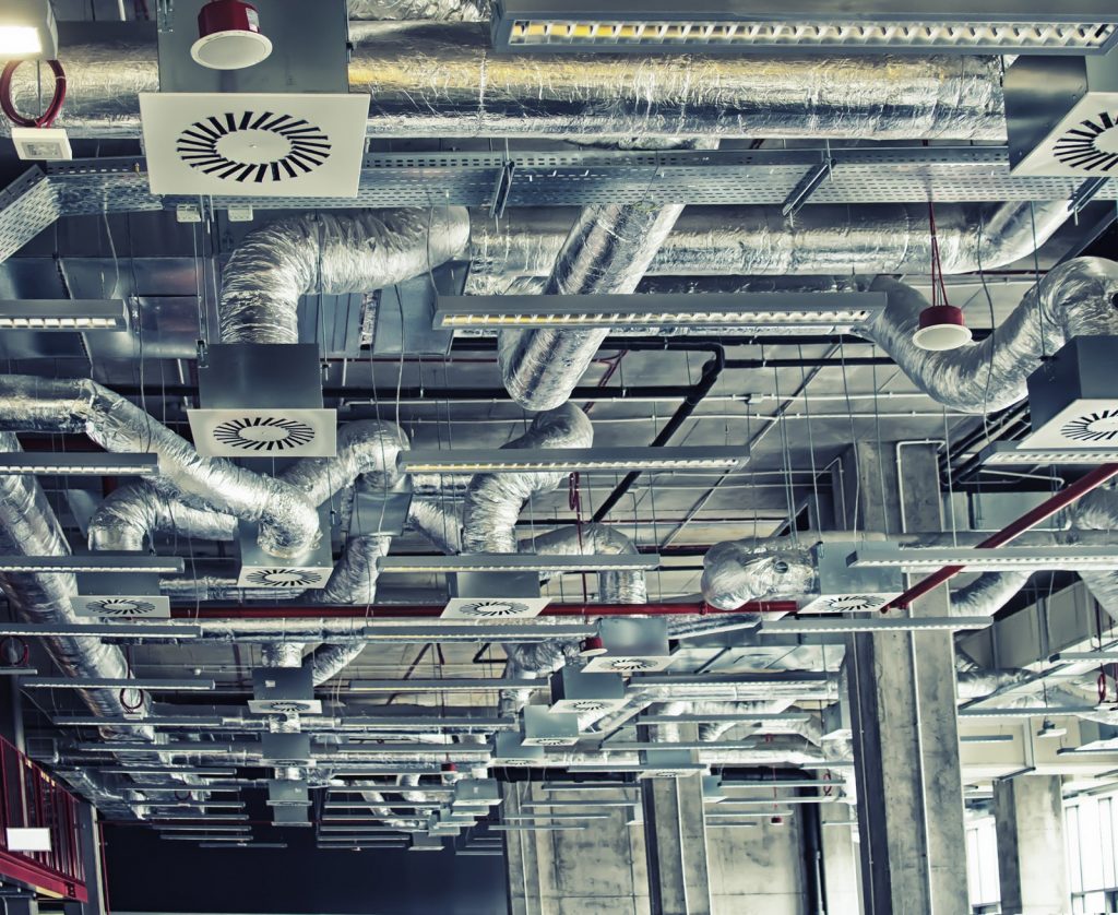 Luchtkanalen geplaatst aan een open plafond in een industriële ruimte